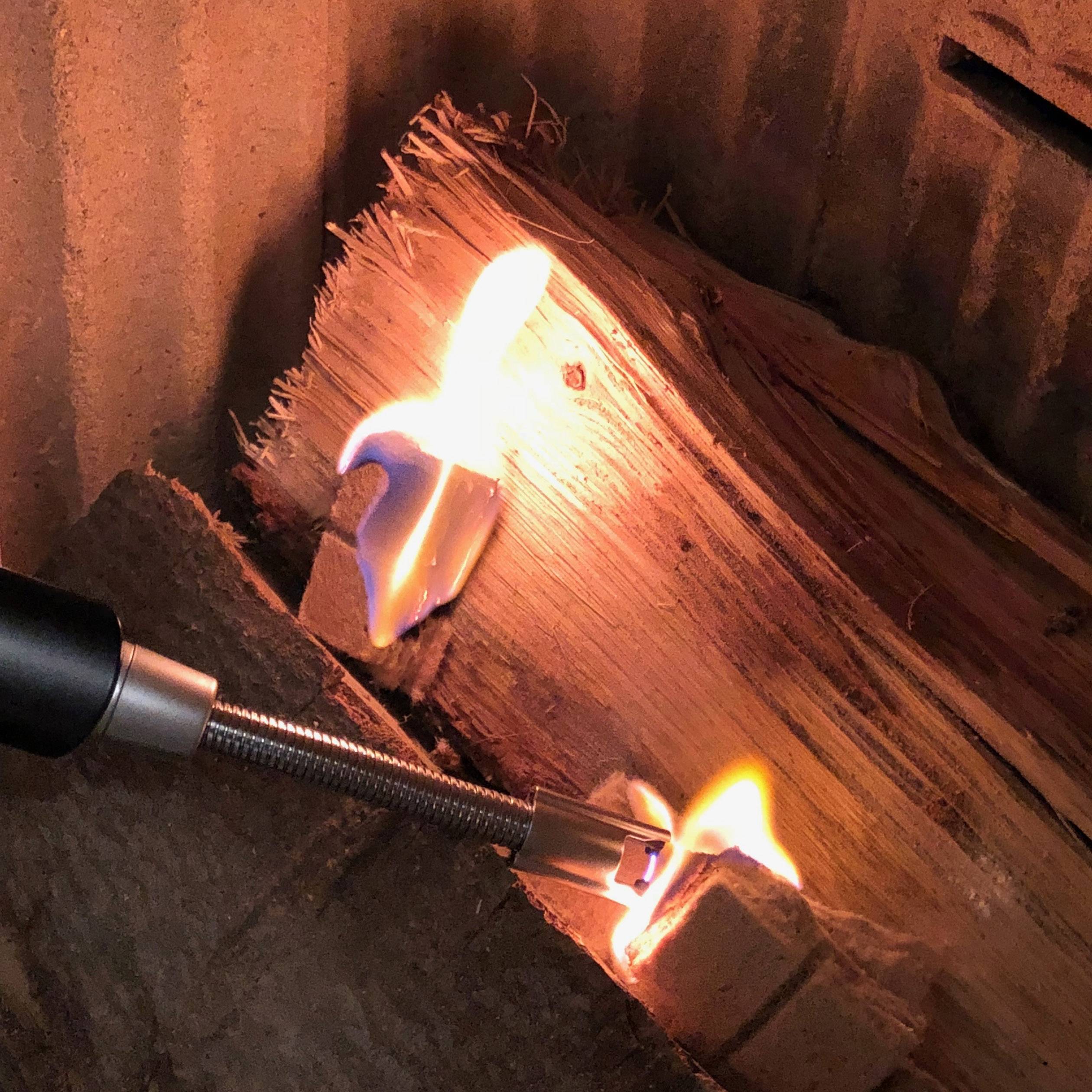 Ein Feuerzeug entzündet einen Stapel Holz in einem Kamin. Flammen beginnen sich auszubreiten und leuchten hell in der Umgebung.