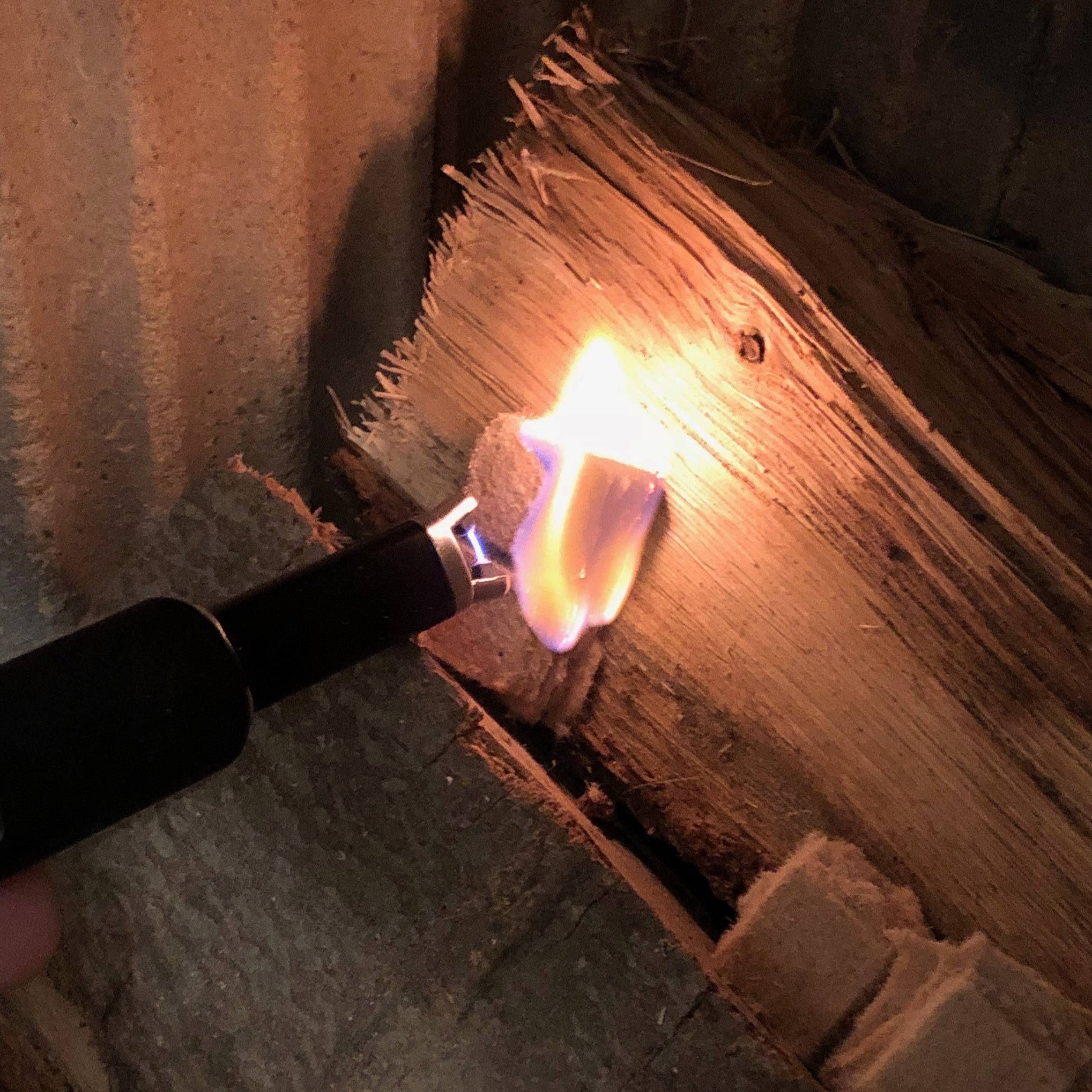 Ein elektrisches Feuerzeug entzündet ein Stück Holz. Die Flamme ist hell und das Holz beginnt zu brennen.