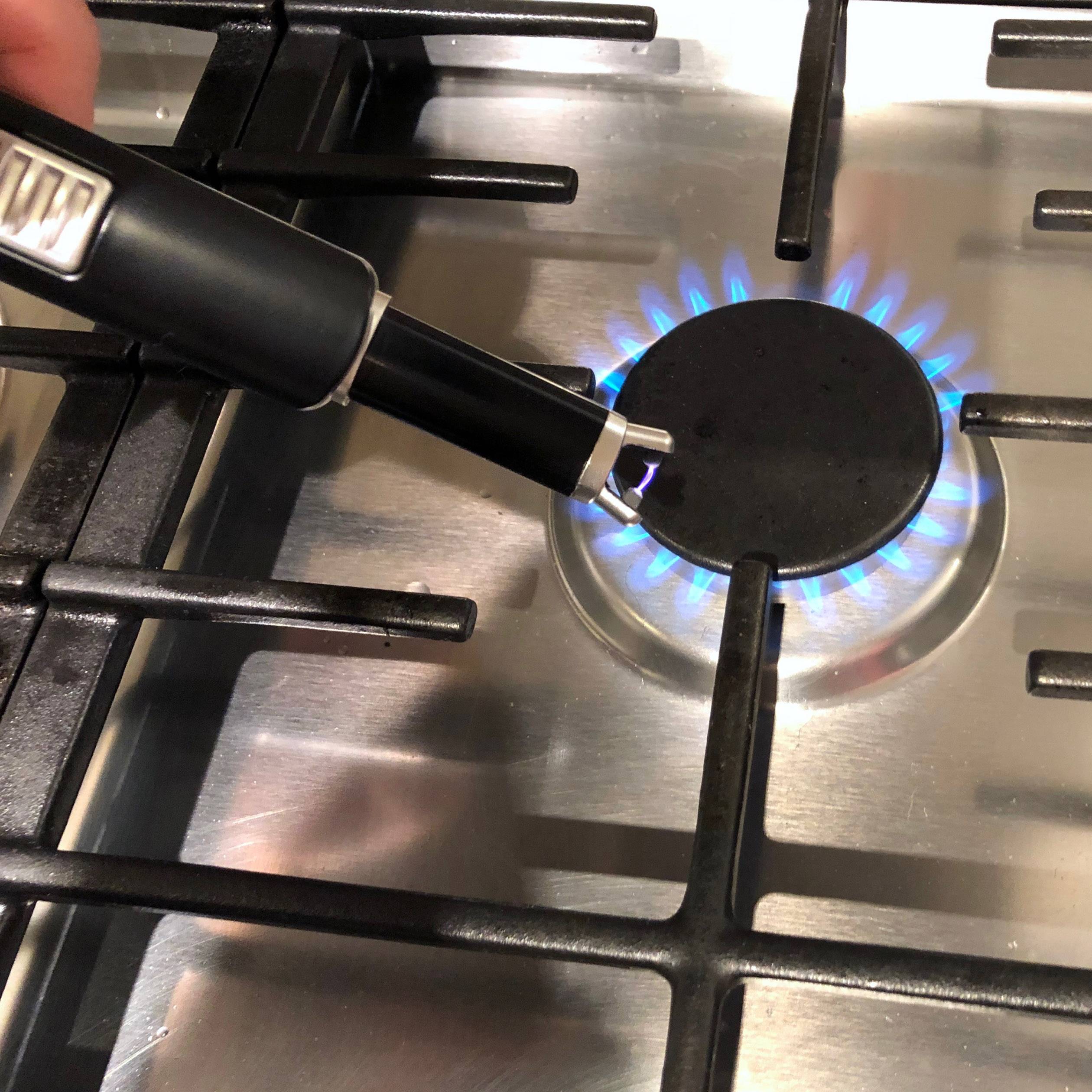 Ein Gasherd wird mit einem Feuerzeug entzündet. Eine blaue Flamme brennt unter einem der Brenner auf dem Herd.