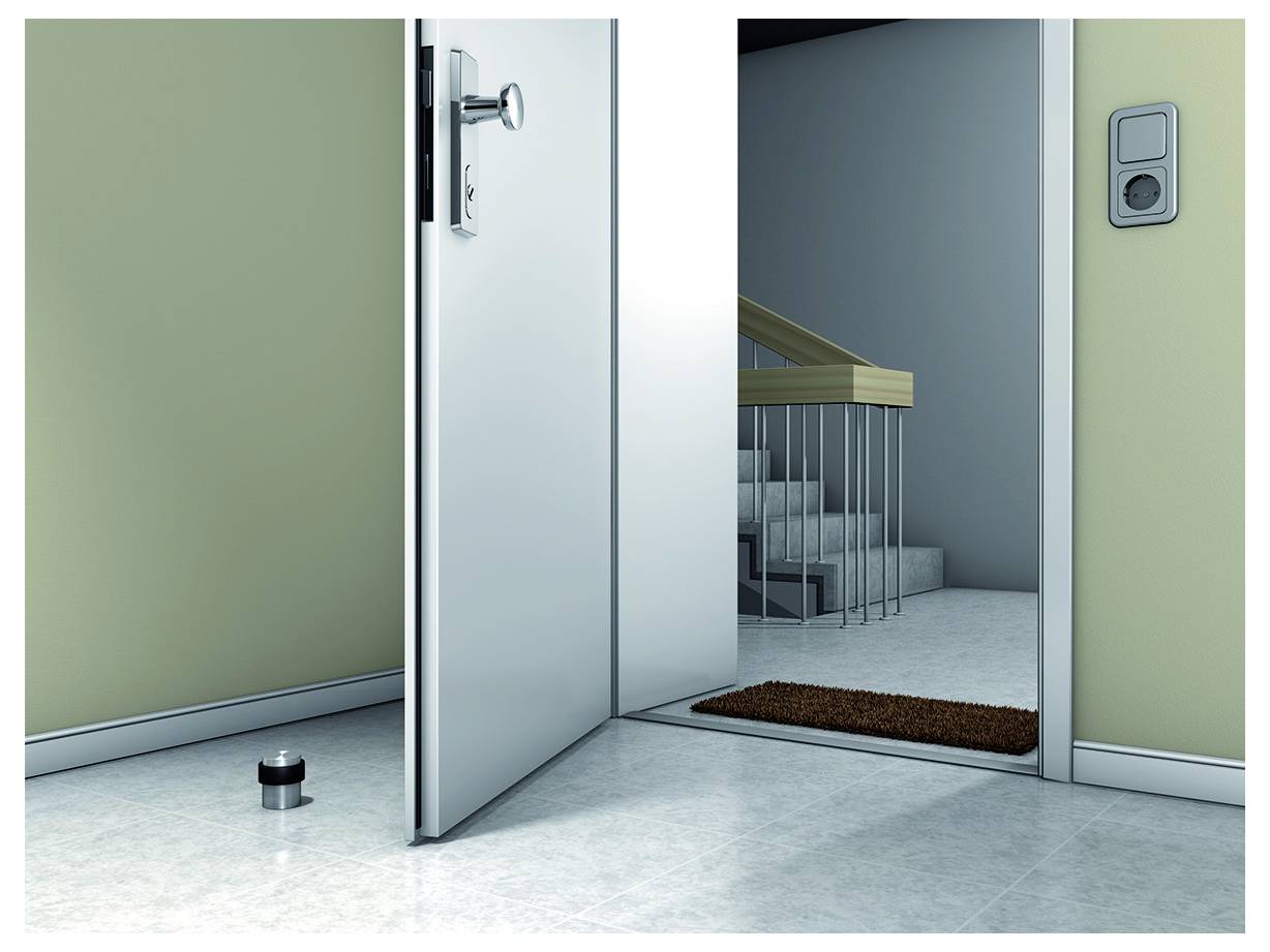 Eine offene Tür führt zu einem hell beleuchteten Flur mit Treppen. Ein Türstopper liegt auf dem Boden. Ein Lichtschalter ist an der Wand angebracht.