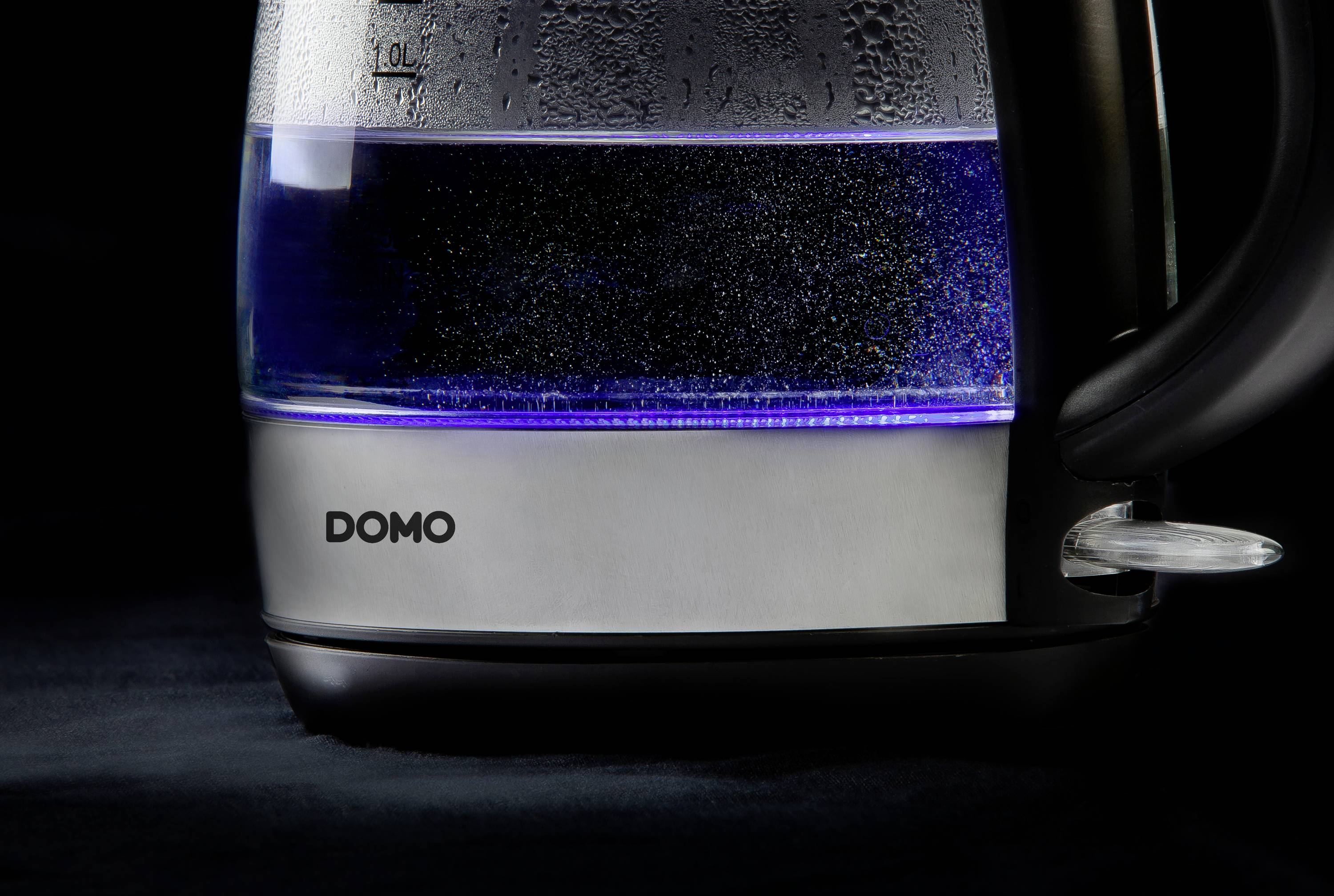 Wasserkessel mit transparentem Behälter, halb voll mit Wasser, auf dunklem Hintergrund. Markennamen 'DOMO' auf dem Metall sichtbar.