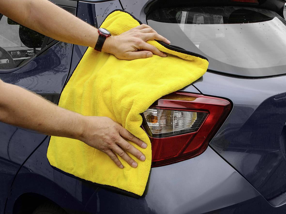 Eine Person reinigt das Rücklicht eines Autos mit einem gelben Tuch. Hände sind auf dem Tuch sichtbar.