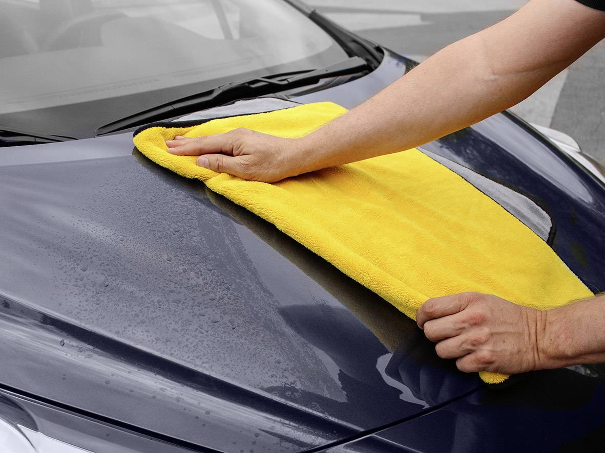 Eine Person wischt mit einem gelben Tuch die Motorhaube eines Autos sauber.