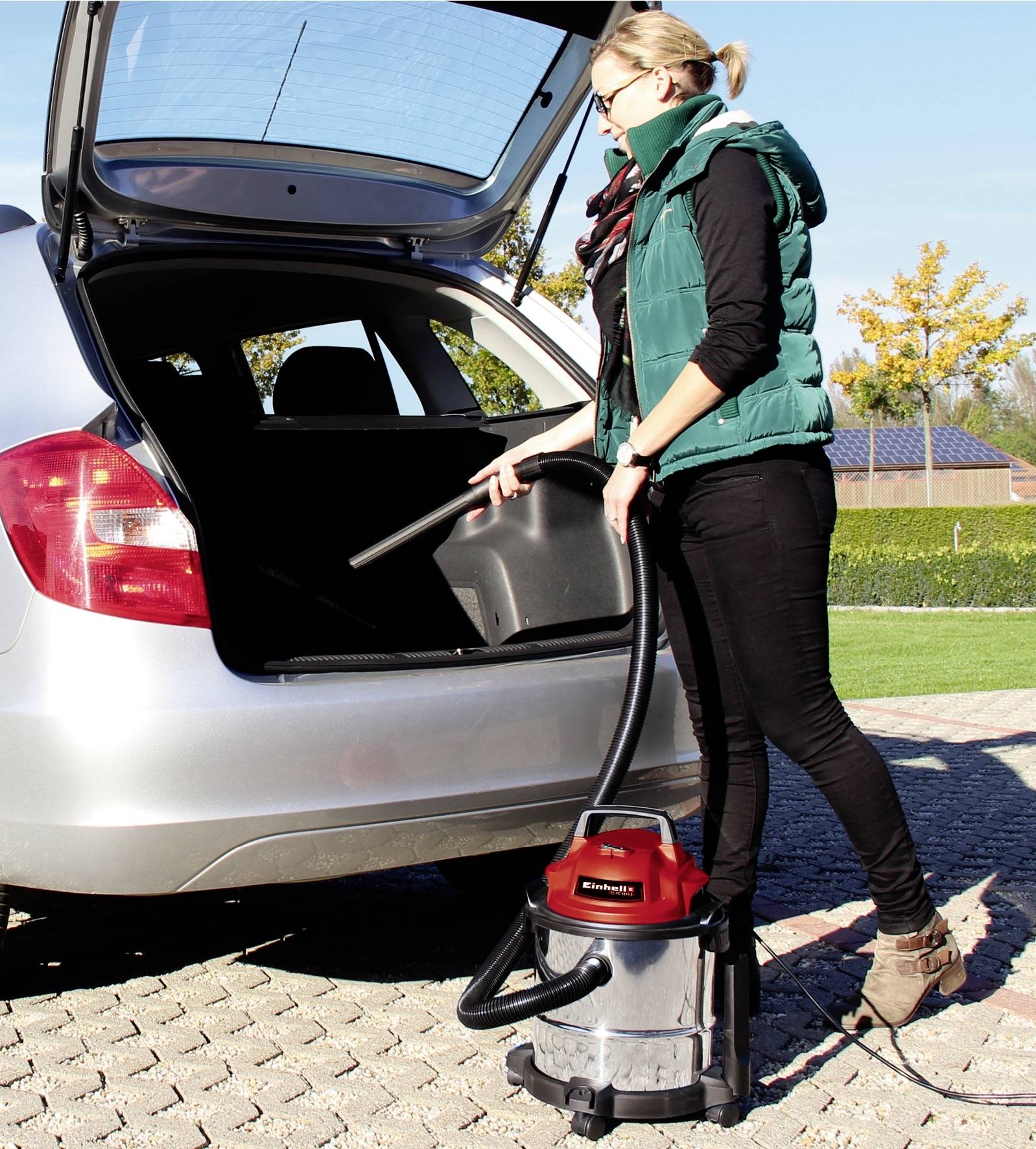 Frau saugt das Innere eines Autokofferraums auf einem Parkplatz mit einem Staubsauger.