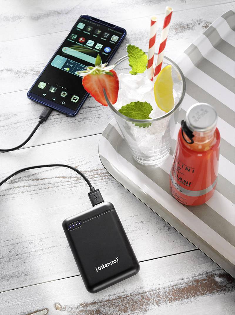 Smartphone lädt über eine Powerbank auf. Daneben ein Tisch mit einem Glas mit Eisgetränk, Erdbeerscheiben und Zitronenscheibe, sowie eine Flasche Saft.