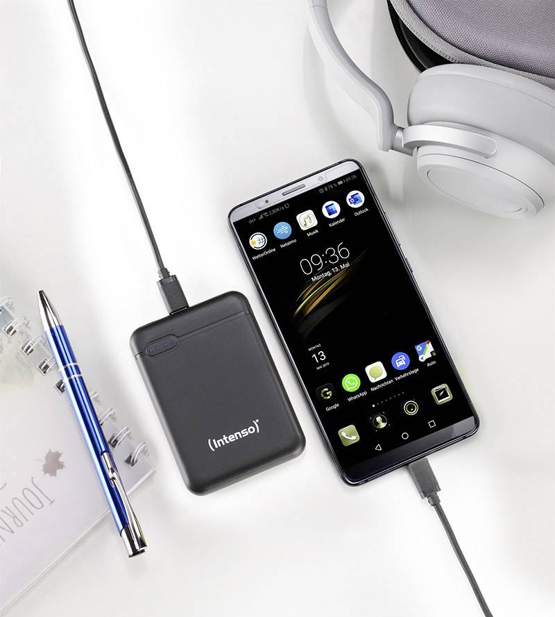Ein Smartphone wird von einer externen Powerbank geladen. Daneben liegen ein blauer Stift, ein Notizbuch und Kopfhörer.