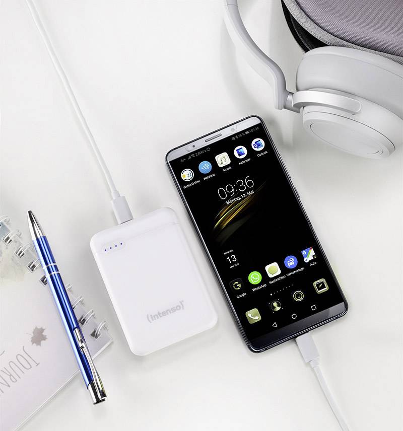 Smartphone und Powerbank auf weißem Hintergrund, verbunden durch Ladekabel; daneben Kopfhörer, Kalender, Kugelschreiber.