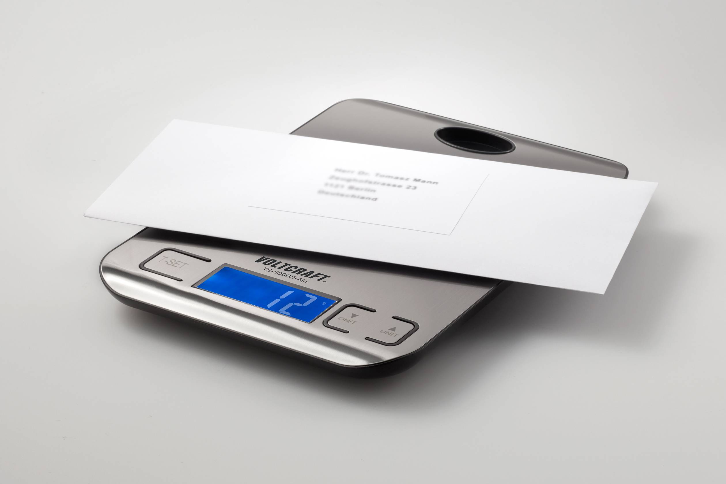 Ein weißer Briefumschlag liegt auf einer digitalen Waage. Die Anzeige zeigt ein Gewicht von 12 Gramm.