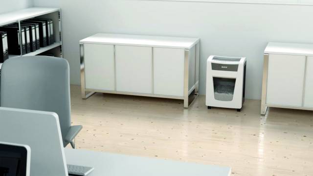 Ein Büro mit Aktenschränken, einem Shredder und einem Tisch mit einem Laptop. Heller Holzboden und weiße Wände.