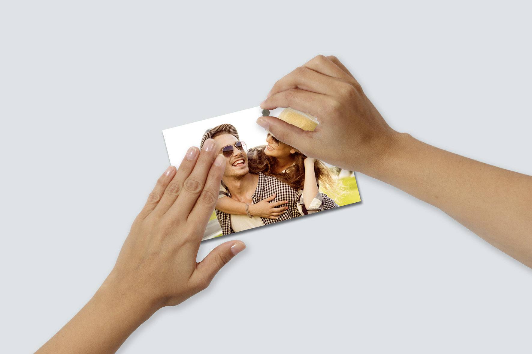 Zwei Hände halten ein Foto von einem lächelnden Paar im Freien. Die Frau umarmt den Mann von hinten.