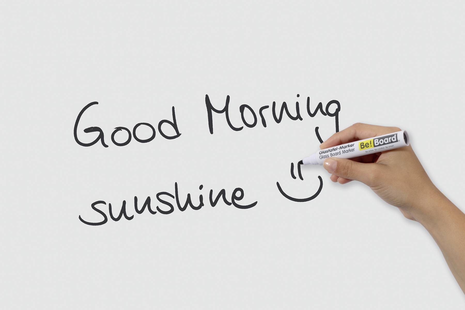 Hand schreibt auf Whiteboard 'Good Morning sunshine :)'.