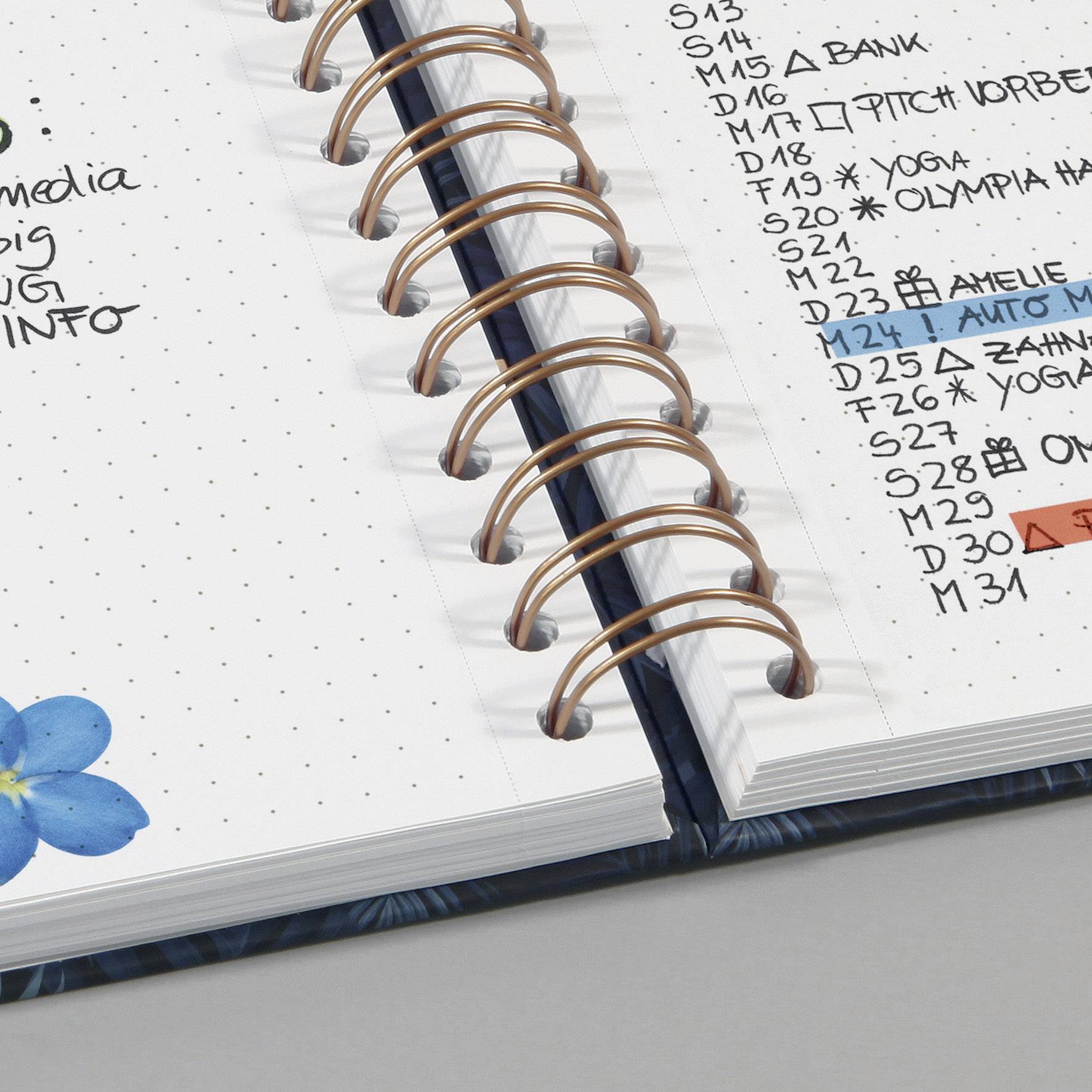 Offener Planer mit handschriftlichen Terminen, Symbolen und blauer Blume am Rand. Enthält Notizen für Arbeit, Bank und Yoga.
