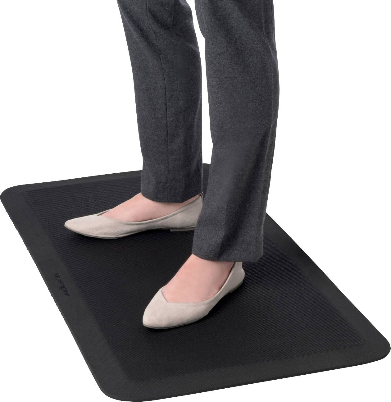 Person steht auf einer schwarzen, rechteckigen Matte, trägt graue Hosen und beige Schuhe.