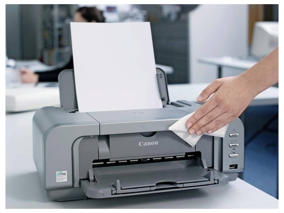 Ein Drucker wird von einer Hand einer Person mit einem Tuch in einer Büroumgebung gereinigt.