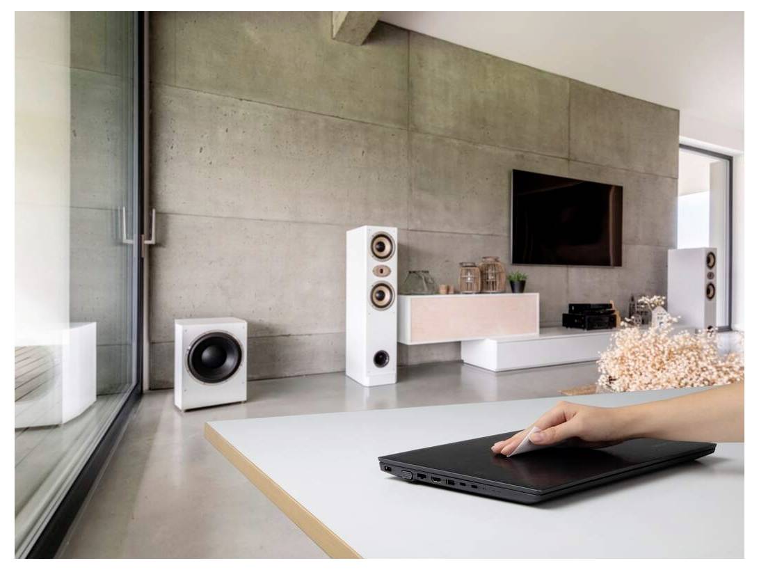 Ein modernes Wohnzimmer mit minimalistischem Design, das einen Fernseher, Lautsprecher und die Hand einer Person zeigt, die auf einem zugeklappten Laptop auf einem Tisch ruht.