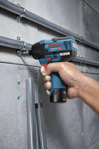 Eine Hand hält einen Bosch Akkuschrauber und befestigt Rohre an einer Betonwand.
