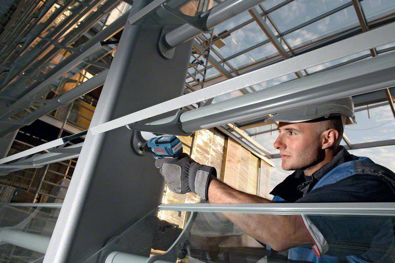 Ein Bauarbeiter mit Schutzhelm verwendet ein Elektrowerkzeug, um eine Metallstruktur in einem modernen Gebäude zu reparieren.