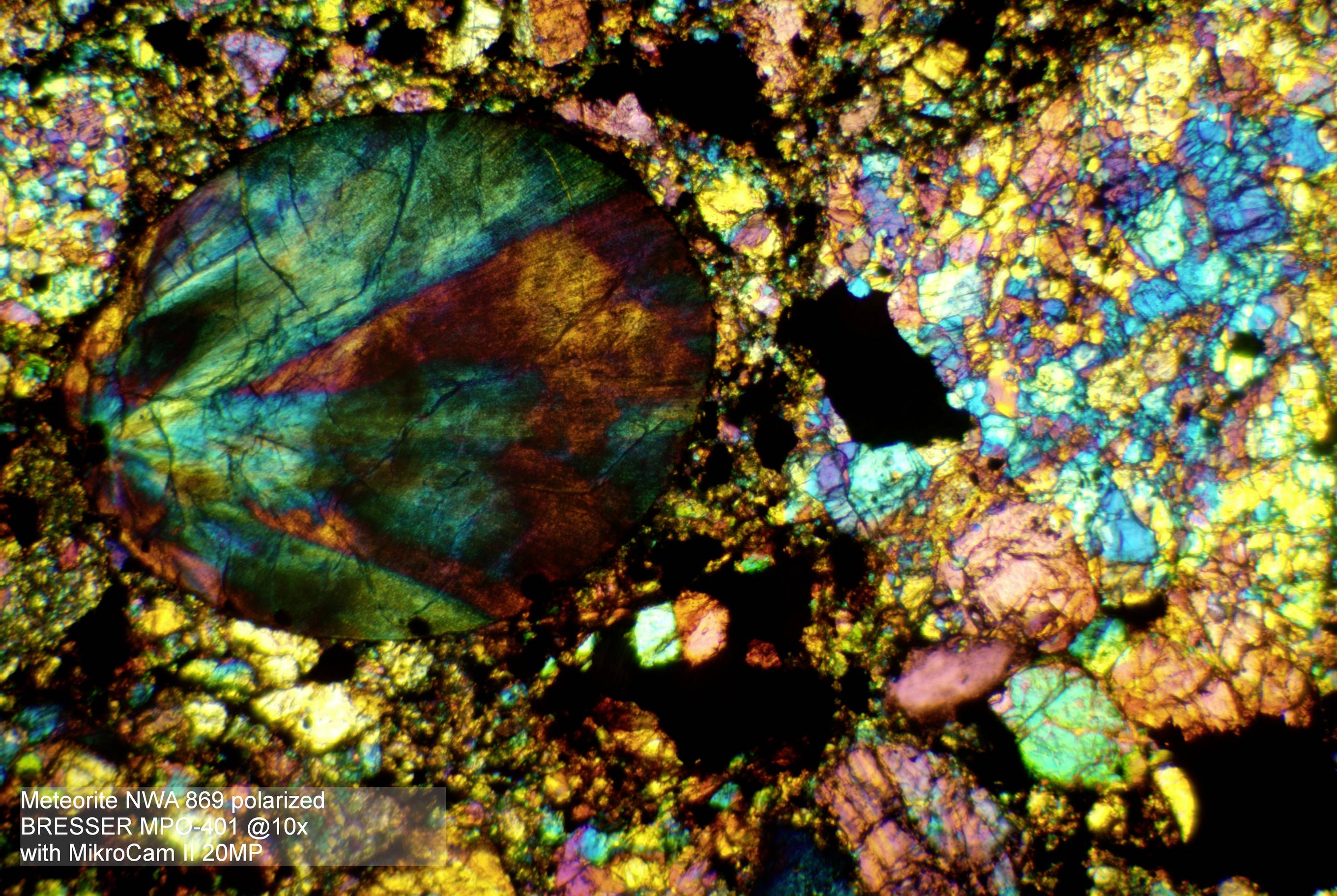 Polarisierte Mikroskopaufnahme eines Meteoriten: bunte mineralische Strukturen mit runden Formen, Text 'BRESSER MikroCam 20 MP'.
