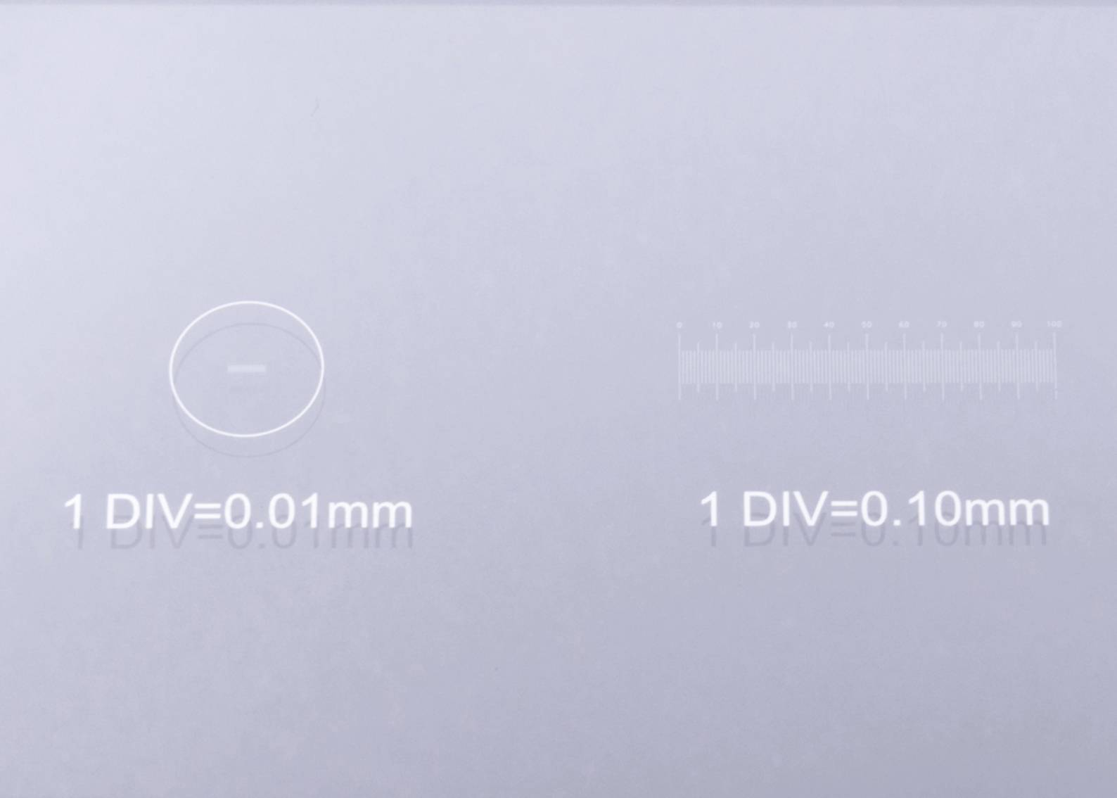Glas-Messinstrument mit zwei Skalen: Links ein Kreis mit '1 DIV=0,01mm', rechts eine Linearskala mit '1 DIV=0,10mm'.