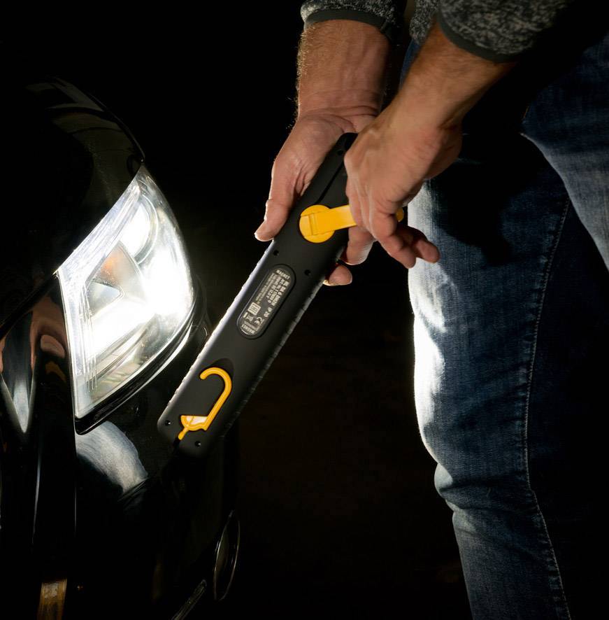 Eine Person überprüft den Luftdruck eines Reifens mit einem digitalen Reifendruckmesser neben einem Auto im Dunkeln.