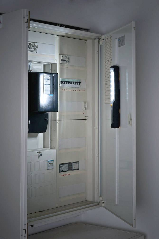 Ein geöffneter Sicherungskasten mit sichtbaren Schaltern und Kabeln an einer Wand. Elektrische Installationen sind zu sehen.
