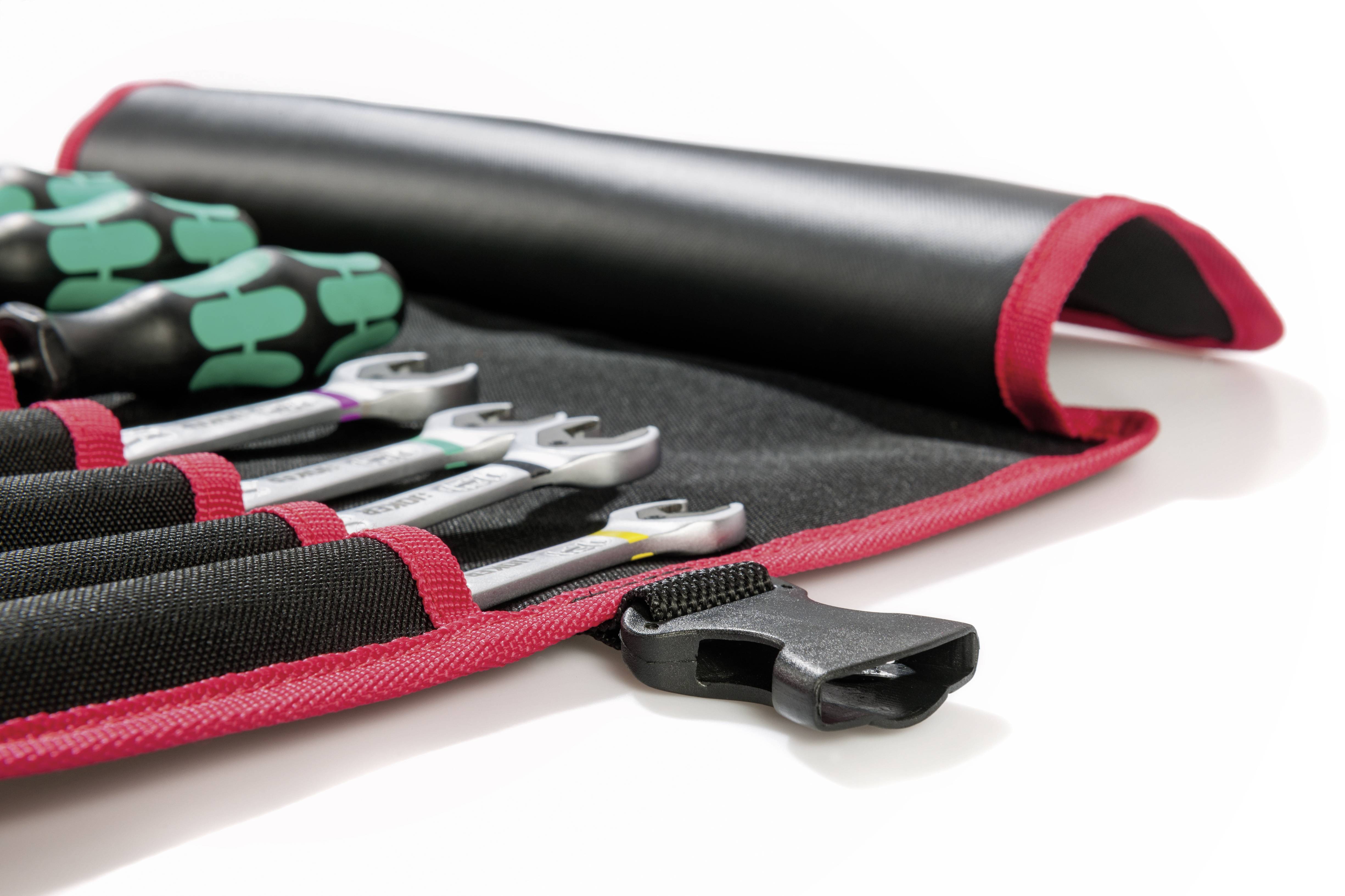 Ein Satz Schraubenschlüssel in einer rot umrandeten Werkzeugtasche mit grünen Griffen, teilweise ausgerollt auf einer weißen Oberfläche.