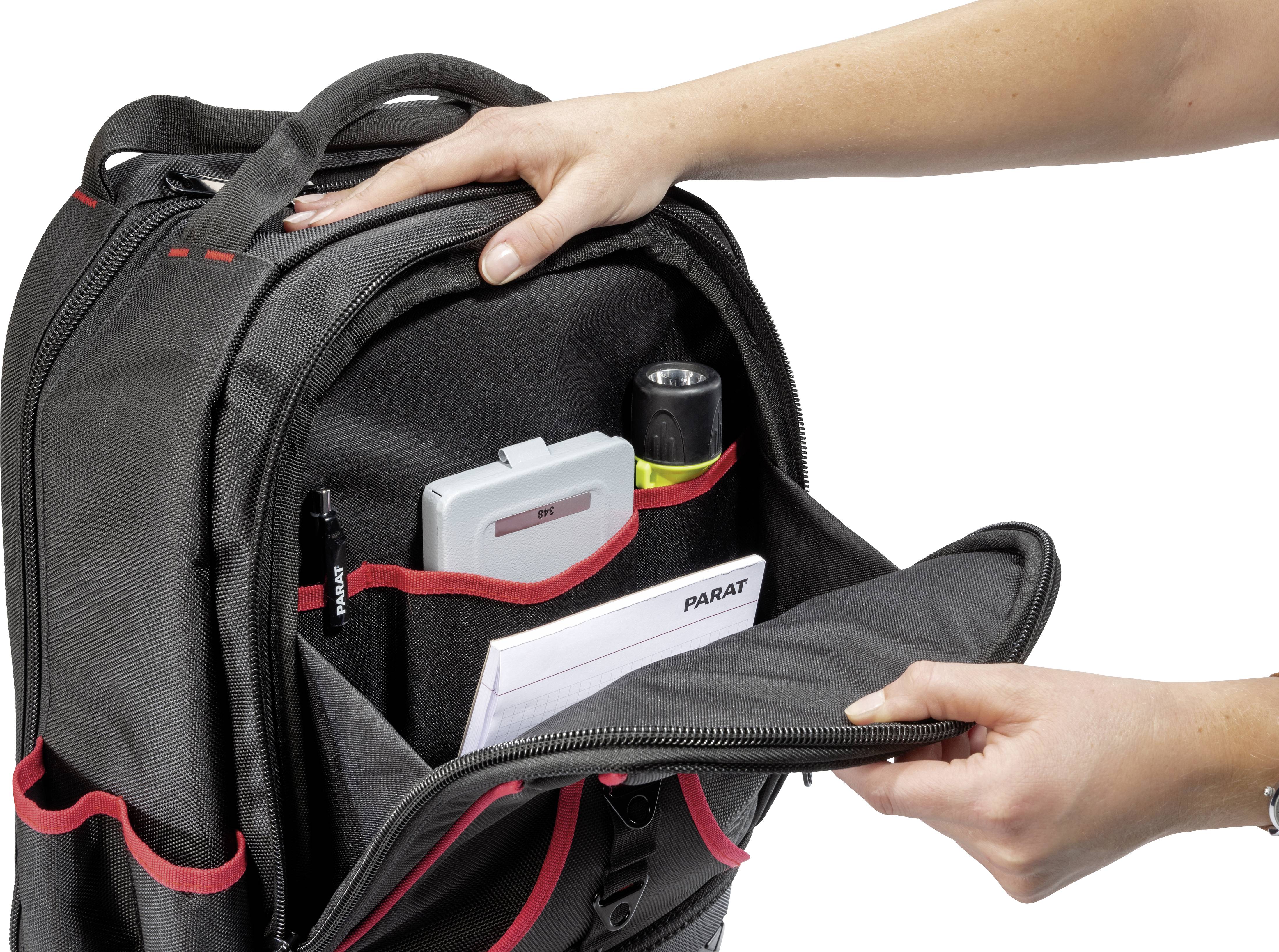 Eine Person öffnet den vorderen Teil eines schwarzen Rucksacks mit roten Akzenten, der Taschen und gefüllte Fächer zeigt.