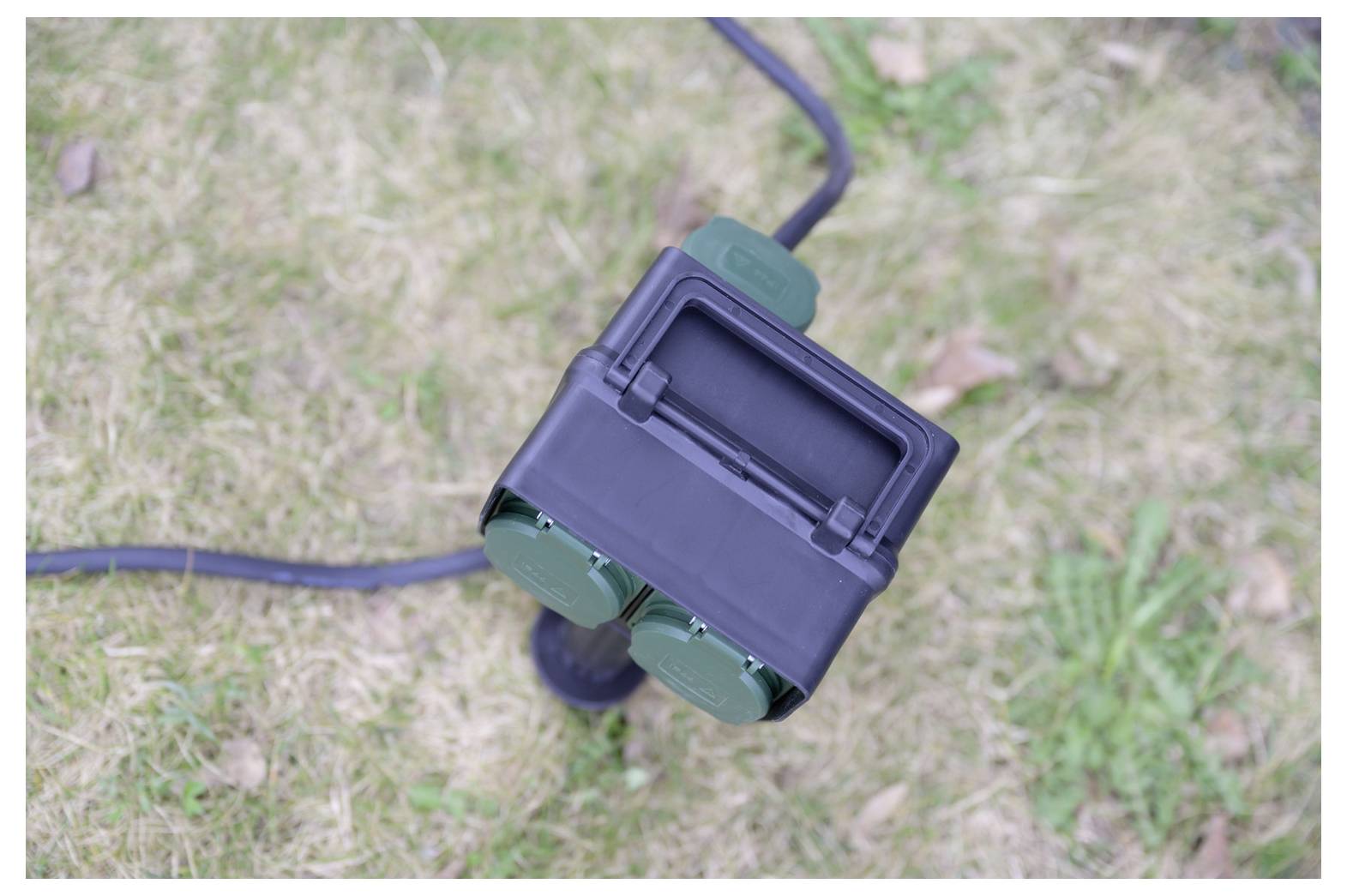 Nahaufnahme eines schwarzen und grünen tragbaren elektrischen Geräts an einem Kabel, das auf Gras liegt.