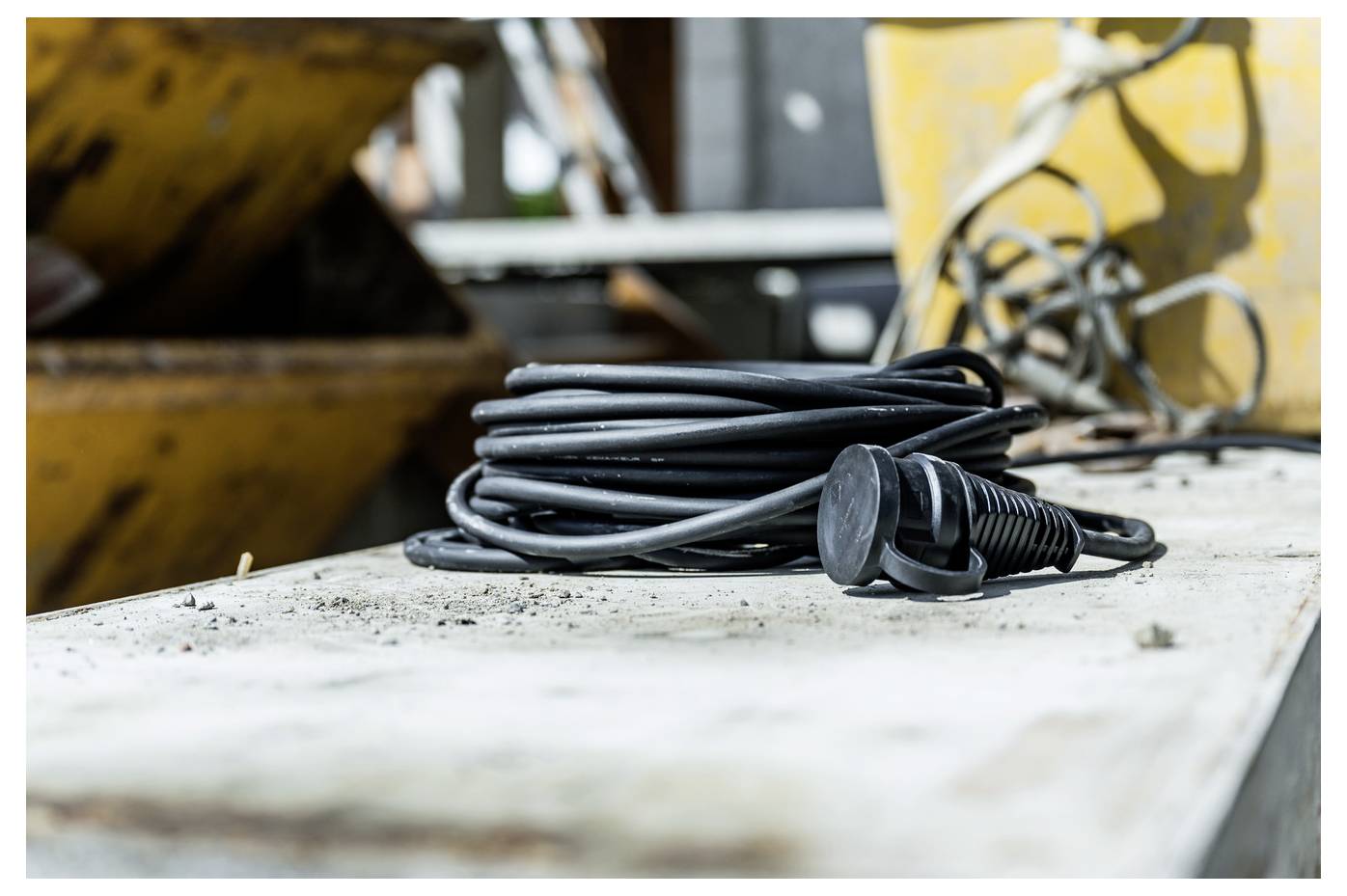 Aufgerolltes schwarzes Elektrokabel mit Stecker, das auf einer staubigen Werkbank in einer Industriewerkstatt ruht.
