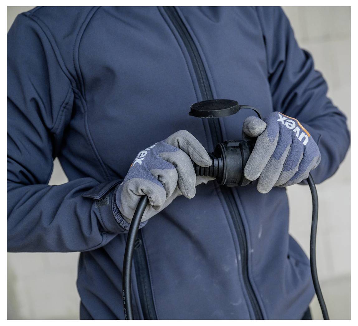 Person mit Handschuhen, die ein schwarzes Stromkabel oder einen Kabelstecker gegen eine schlichte Wand hält und überprüft.