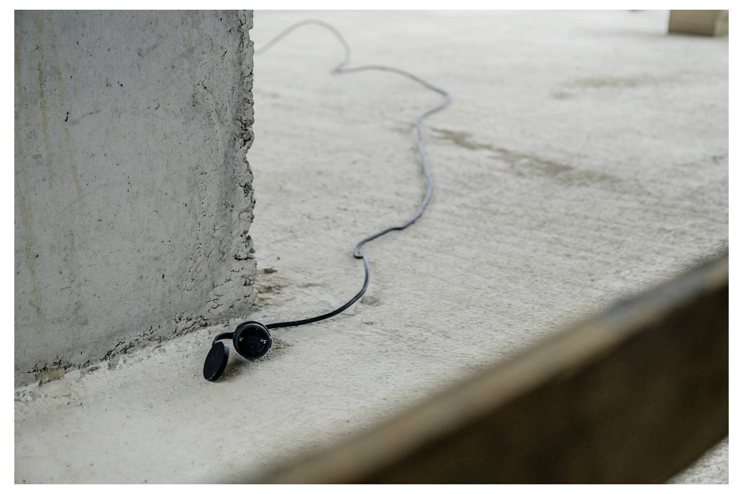 Schwarze kabelgebundene Ohrhörer liegen auf einem Betonfußboden neben einer rauen Wand, wobei sich das Kabel in den Hintergrund erstreckt.