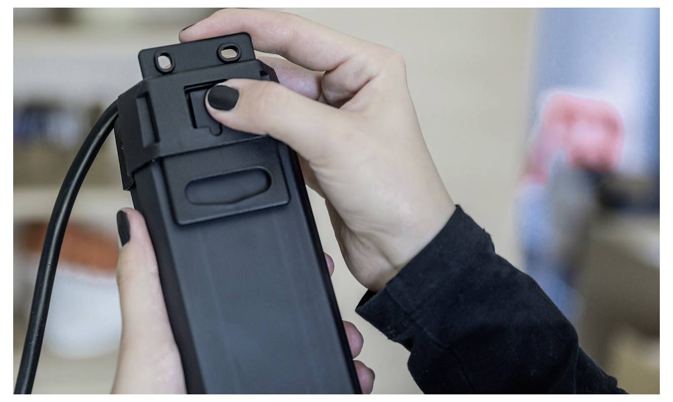 Hände, die ein schwarzes Batteriepaket in ein Gerät einsetzen, wahrscheinlich zum Laden oder Stromversorgung.