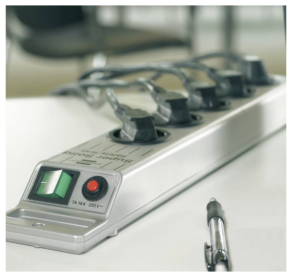 Ein silberner Steckerleistenblock mit mehreren Steckdosen, grünem Ein-/Ausschalter und rotem Rücksetzer auf einem weißen Tisch, mit einem Stift daneben.