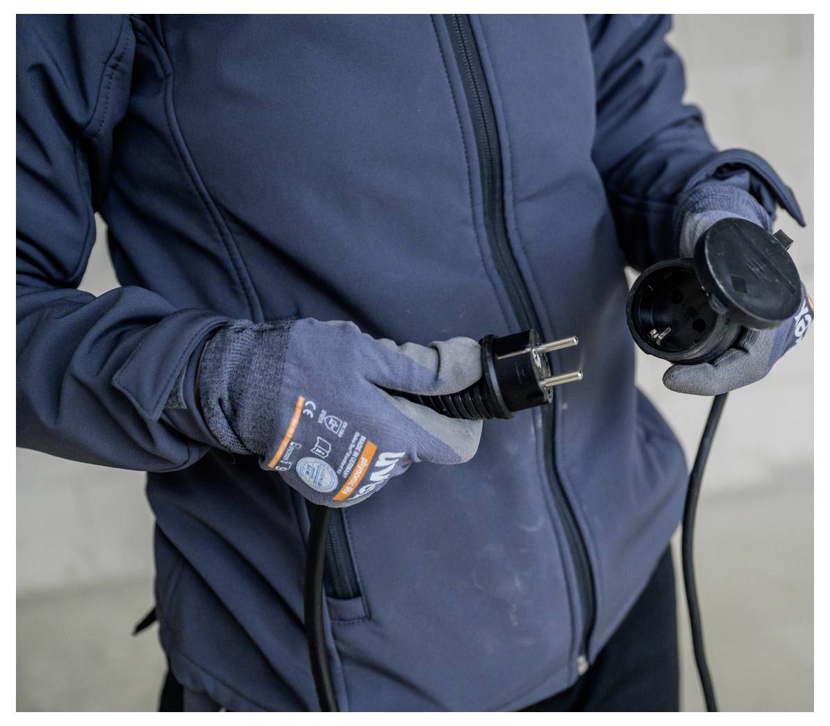 Person in Handschuhen, die einen zweipoligen Stromstecker und die entsprechende Steckdose hält, was auf die Überprüfung oder den Anschluss von Stromausrüstung hindeutet.
