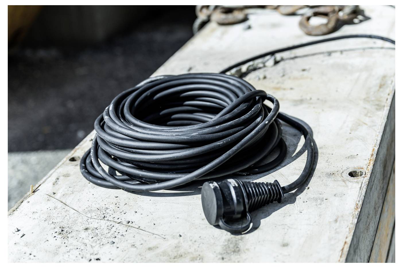 Aufgerolltes schwarzes Kabel mit einem Stecker, das auf einer abgenutzten weißen Arbeitsfläche ruht.