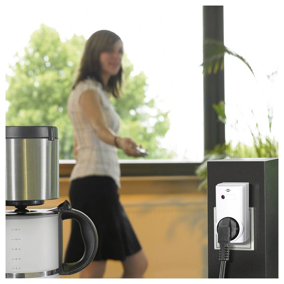 Büroküche mit einer Frau, die sich in der Nähe einer Kaffeemaschine bewegt, und einer angesteckten Steckdose im Vordergrund.