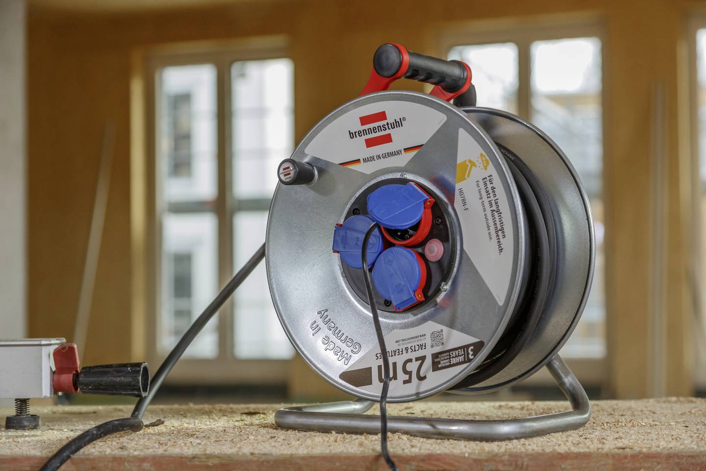 Eine Kabeltrommel steht auf einer Holzoberfläche in einem Raum mit großen Fenstern.