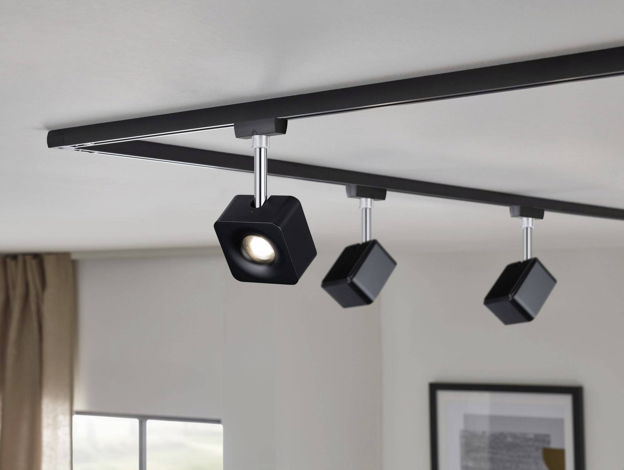 Schwarzes Schienensystem an der Decke mit drei verstellbaren quadratischen LED-Leuchten; modernes Innenraumdesign.