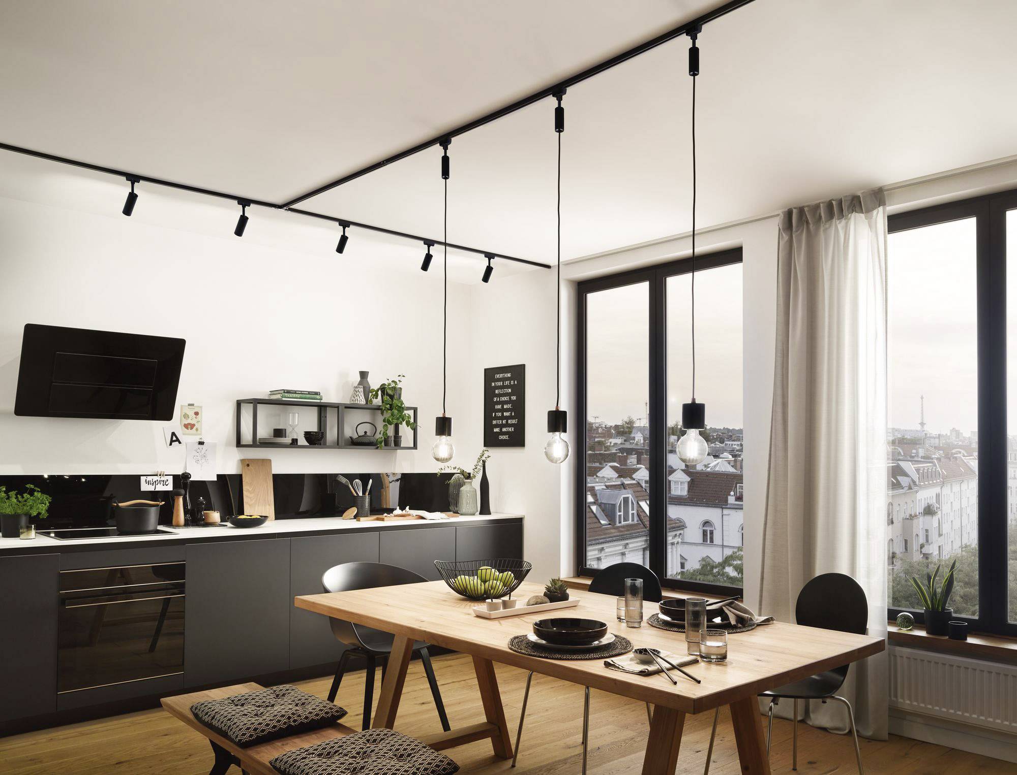 Moderne Küche mit Esstisch und Pendelleuchten, großes Fenster mit Stadtblick im Hintergrund. Tisch mit Geschirr und grünen Äpfeln dekoriert.