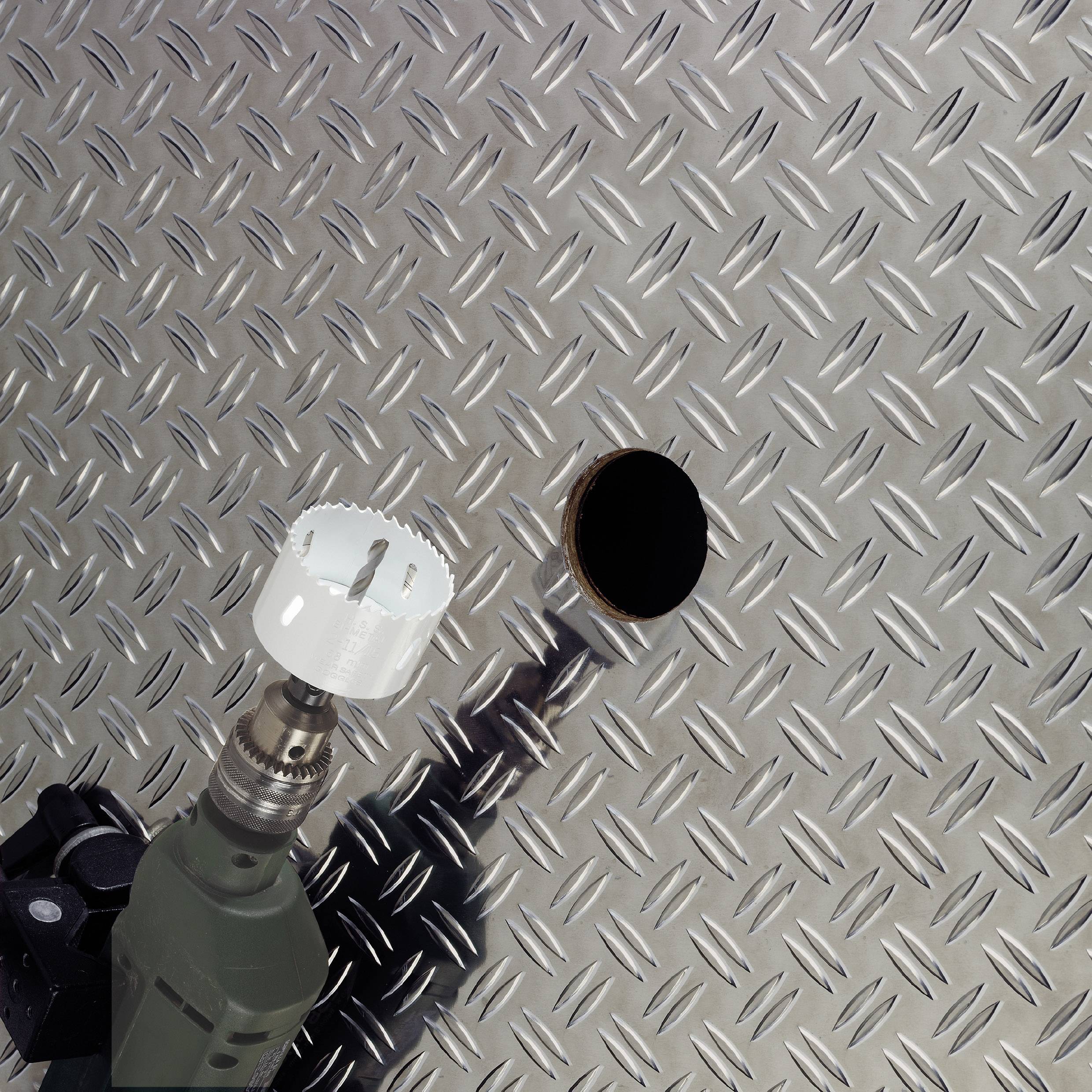 Eine Bohrmaschine mit Lochsäge hat ein Loch in ein diamantförmiges Metallblech gebohrt.