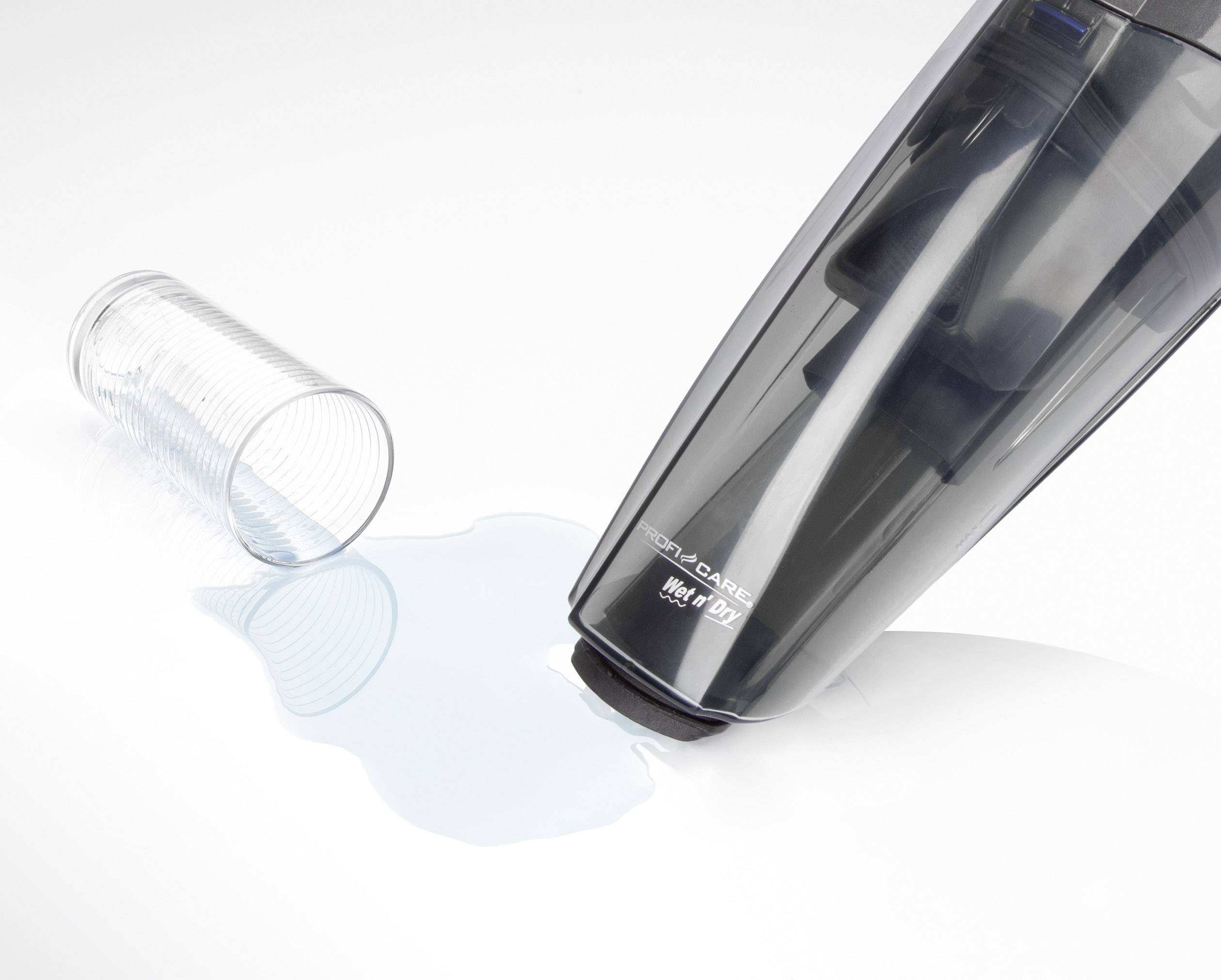 Ein Handstaubsauger saugt verschüttetes Wasser von einer glatten Oberfläche auf. Daneben ein umgefallenes Glas.