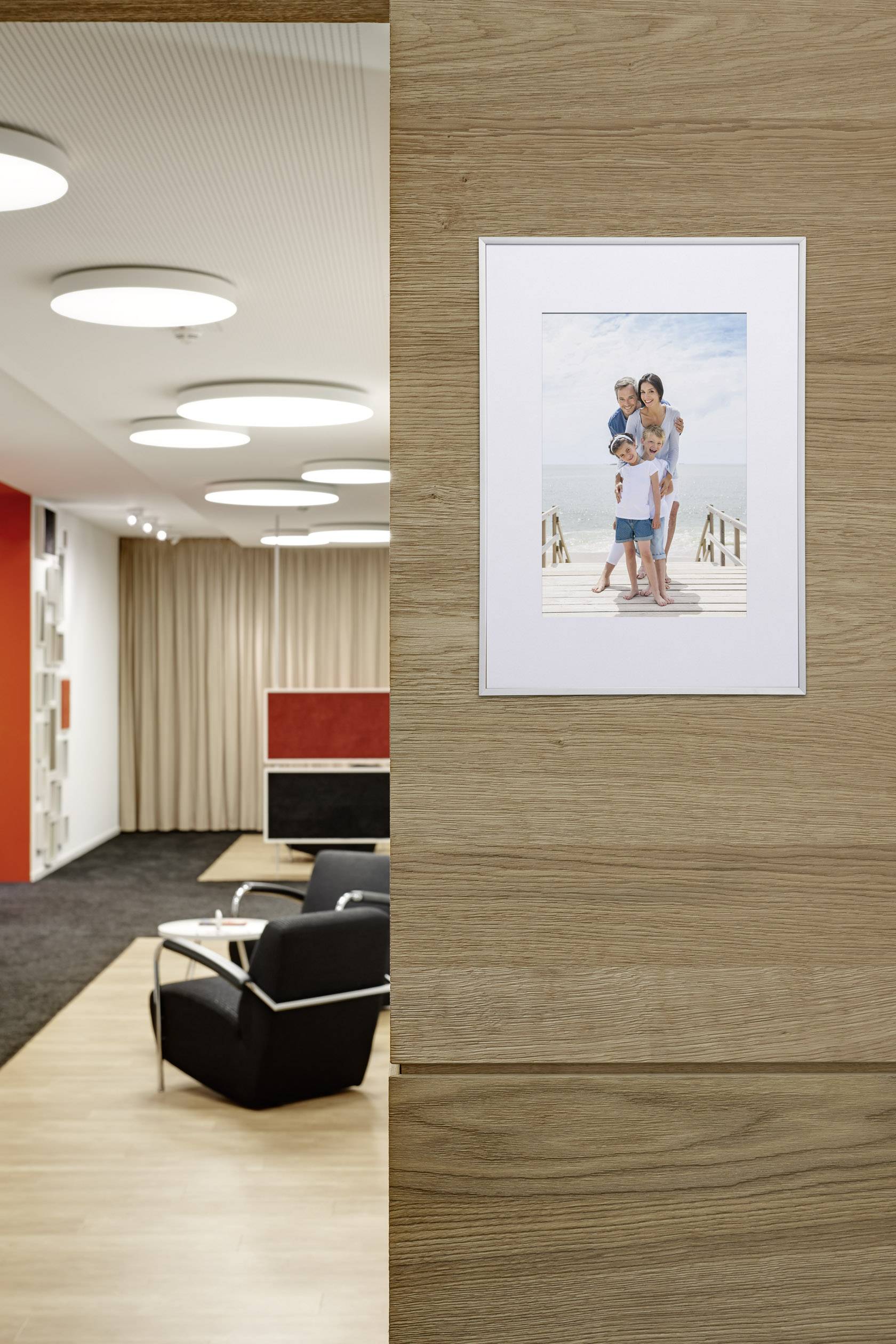Ein Wohnzimmer mit Holzwänden, schwarzen Sesseln und einem gerahmten Foto einer Familie am Strand an der Wand.