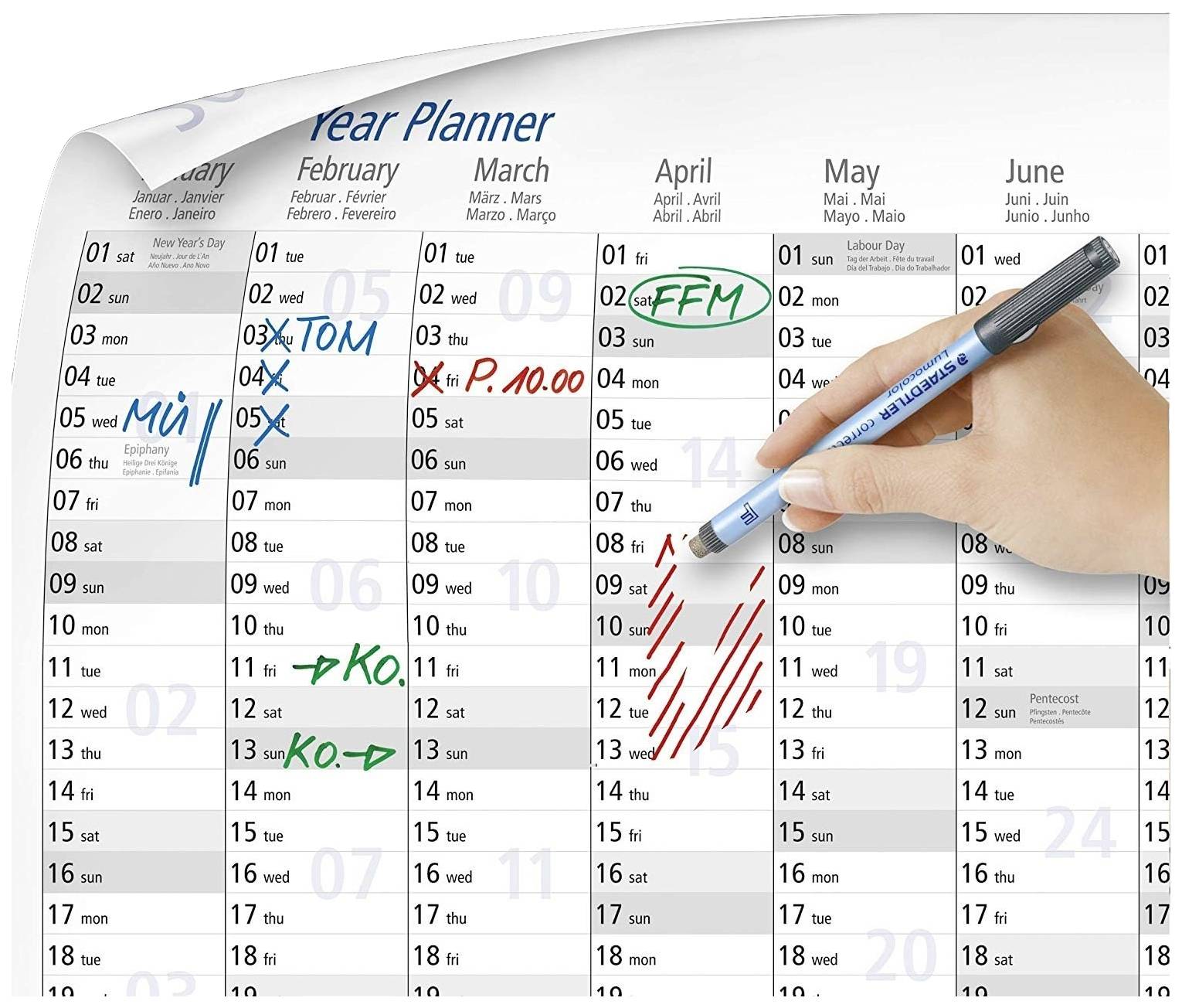 Jahresplaner mit handschriftlichen Notizen: 'MÜ', 'TOM', 'FFM', 'P.10.00', 'KO'. Eine Hand hält einen blauen Stift, markiert Rot.