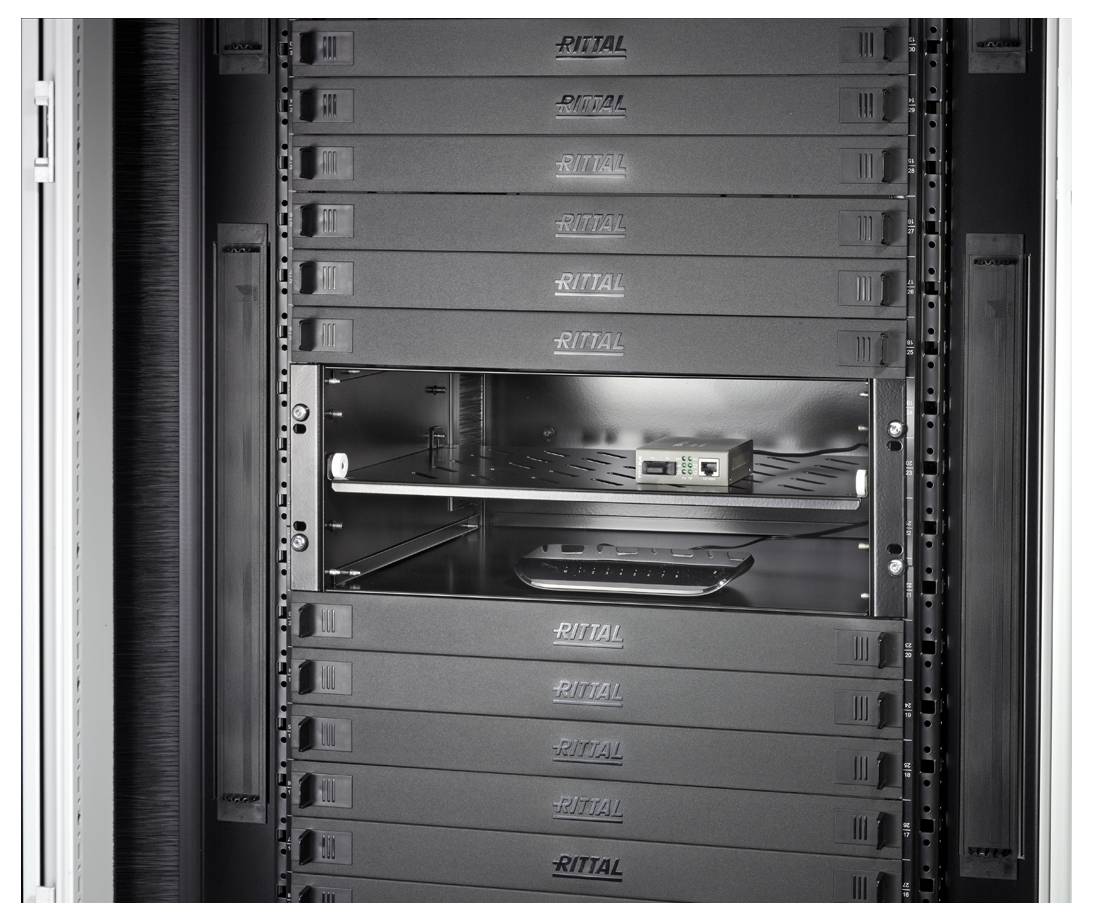 Ein Serverraum mit mehreren schwarzen Servern in einem Gestell. Ein Fach ist leer, das Regal darunter zeigt einige Kabel und ein kleines Gerät.