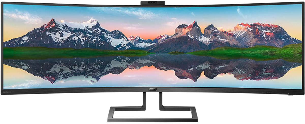 Ein Ultra-Wide-Monitor zeigt ein Panorama von Bergen mit schneebedeckten Gipfeln und einem farbenfrohen Sonnenuntergang, der sich im Wasser spiegelt.