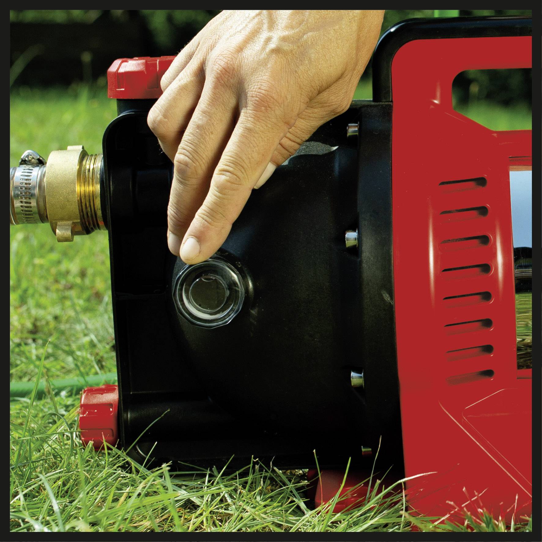 Eine Hand bedient eine rote Wasserpumpe im Gras, um Wasser aus einem Behälter abzulassen.