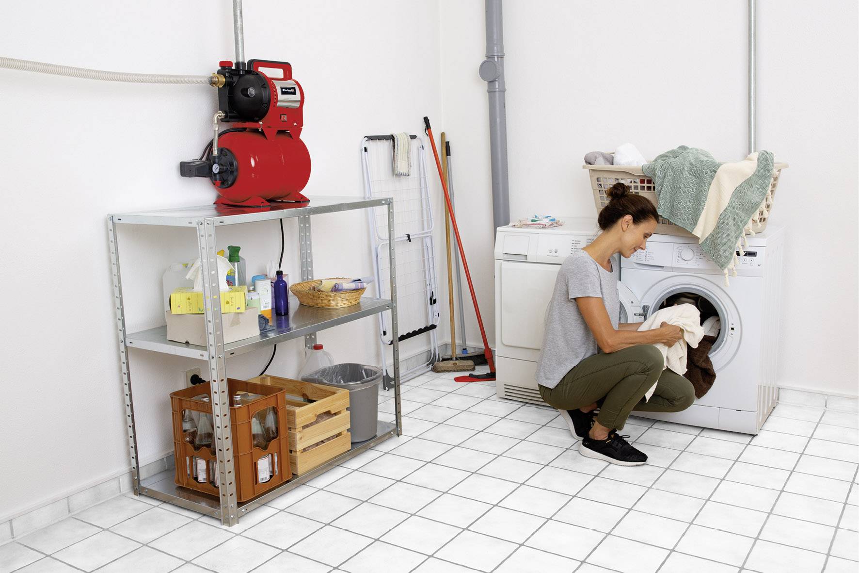 Eine Person belädt eine Waschmaschine in einem hellen Hauswirtschaftsraum. Regale enthalten Reinigungsmittel und andere Haushaltsgegenstände.
