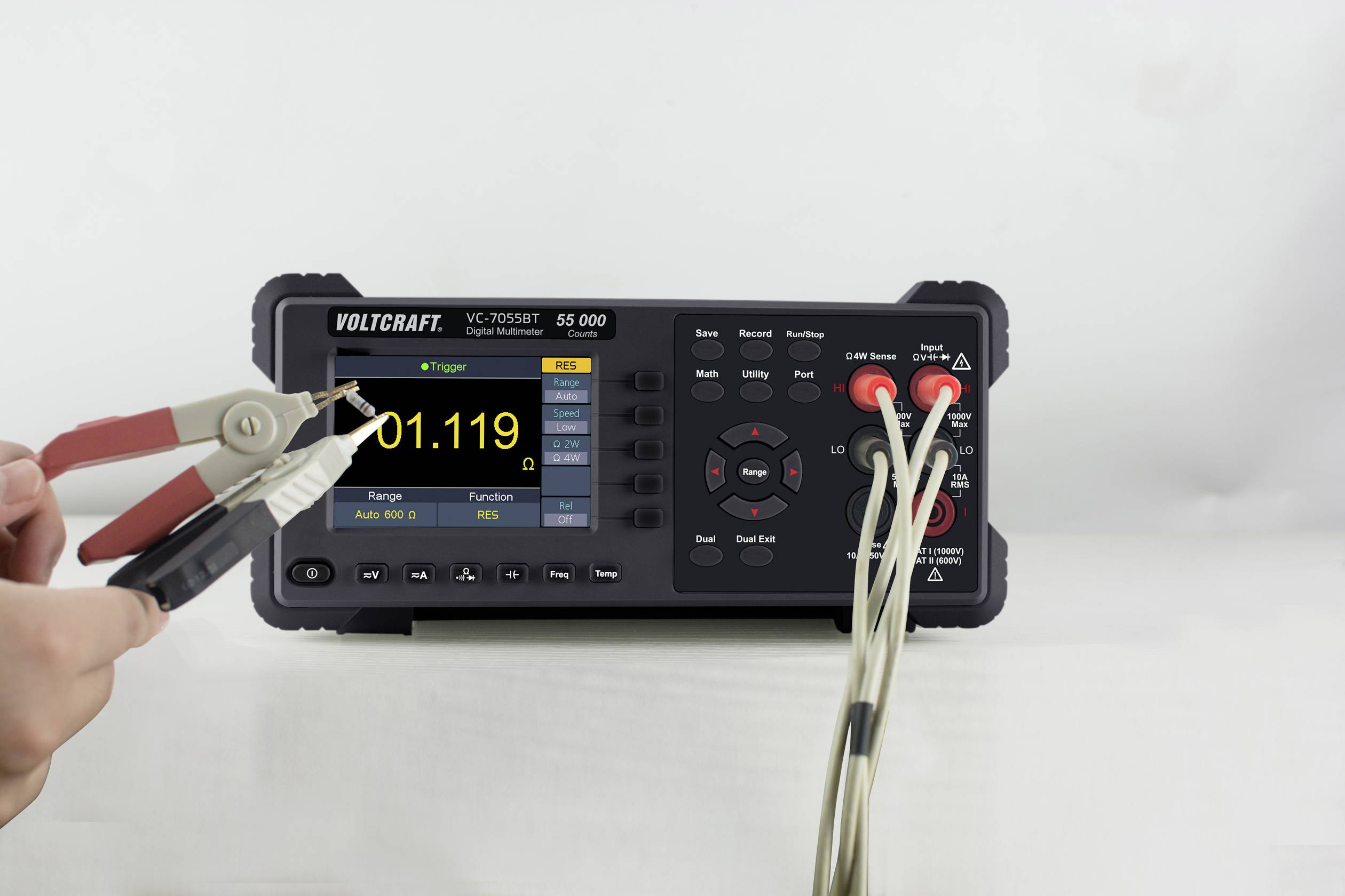 Eine Person hält Messleitungen an einem digitalen Multimeter, das Spannungswerte anzeigt. Auf dem Bildschirm steht '01,119'.