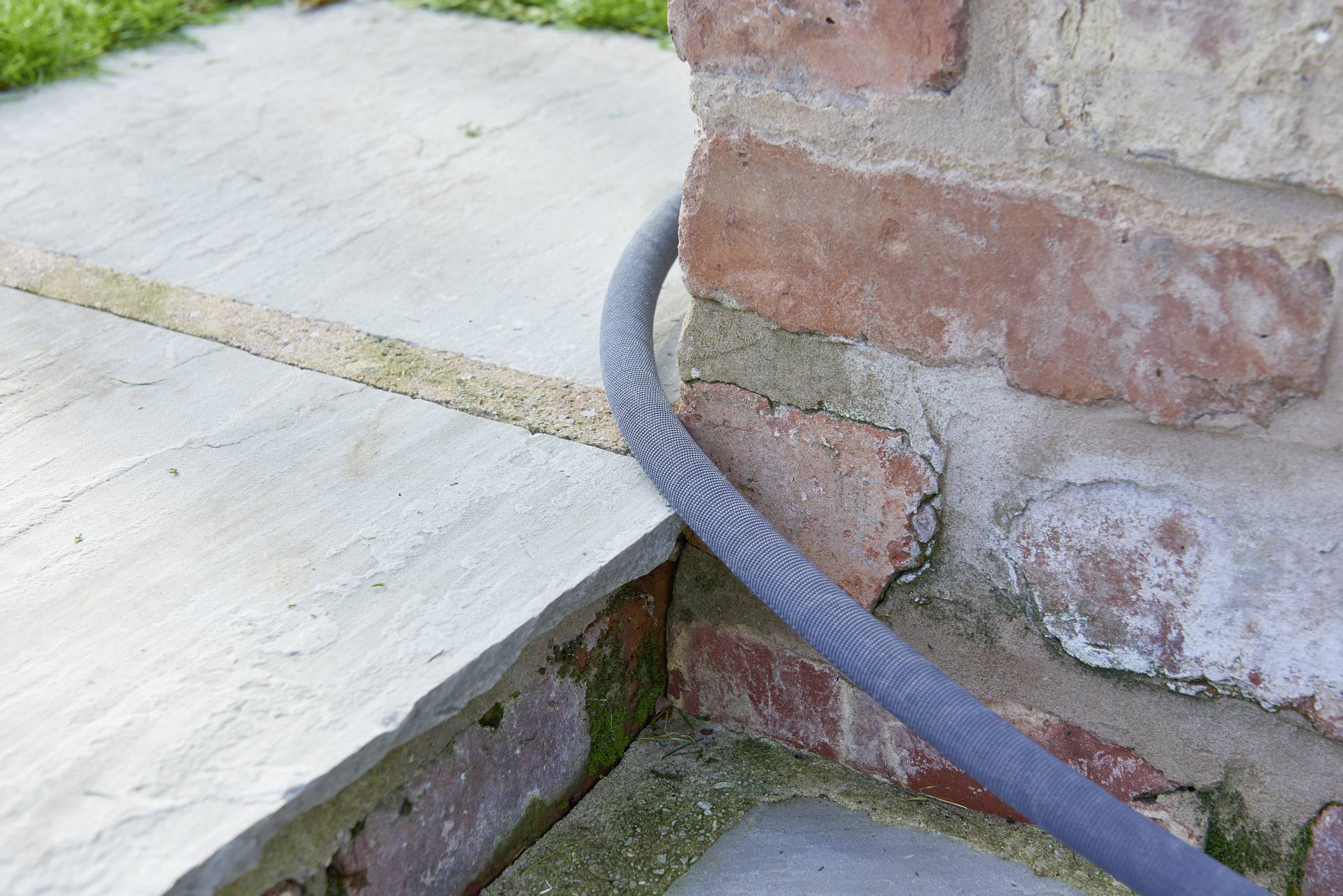 Ein grauer Schlauch verläuft über einen Randstein und entlang einer roten Backsteinmauer im Freien.