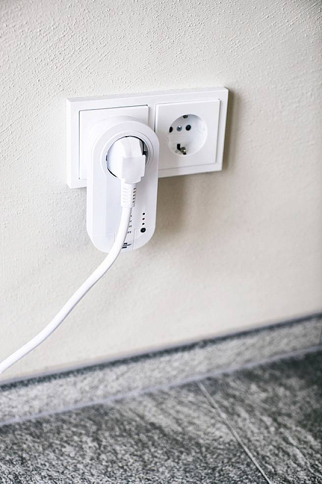 Ein weißer Steckeradapter ist in eine Wandsteckdose eingesteckt. Ein Kabel führt vom Adapter weg.